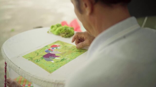 Elderly asian artisan carefully hand stitching a colorful traditional pattern on an embroidery hoop