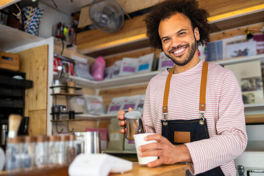 Smiling barista serving takeaway coffee at small kiosk