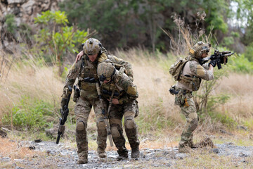 Fototapeta premium Soldier carries injured comrade over rocky terrain