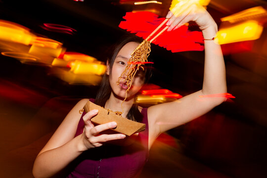 Asian woman eating street noodles at night market scene