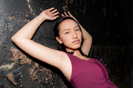 Asian woman posing at night against dark textured wall