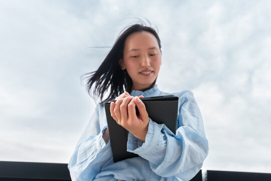 Gen Z asian woman holding tablet outdoors under sky