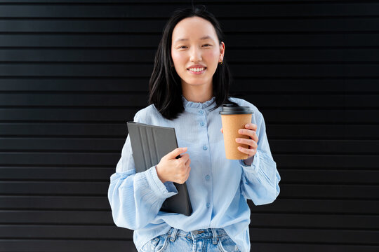 Gen Z Asian woman holding tablet and coffee outdoors