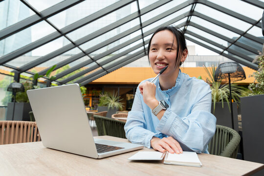 Gen Z Asian woman planning on laptop in rooftop cafe