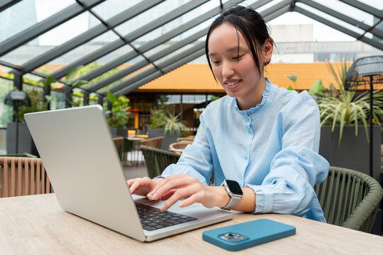 Gen Z Asian woman working on laptop at rooftop cafe