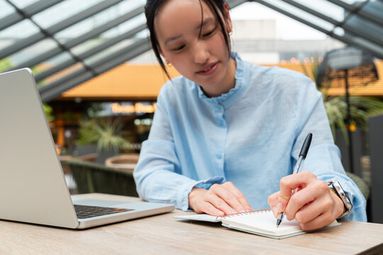 Gen Z Asian woman taking notes with laptop at cafe