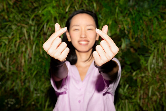 Gen Z Asian woman showing finger heart gesture outdoors