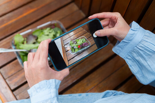 Person photographing fresh salad with smartphone on table