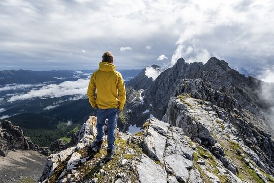 Hiker at the summit of the Westliche T&ouml;rlspitze, in the background cloudy feslige summit of the East T&ouml;rlspitze and Wettersteinwand, Wetterstein Mountains, Garmisch Partenkirchen, Bavaria, Germany