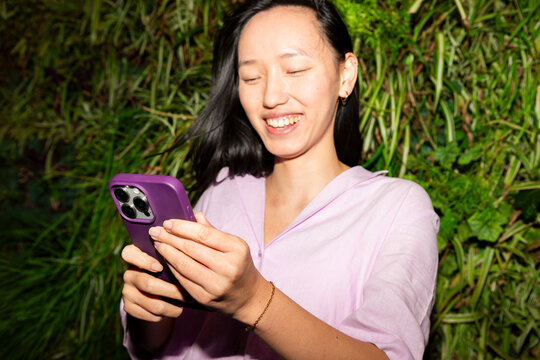 Gen Z Asian woman Smiling while using smartphone outdoors