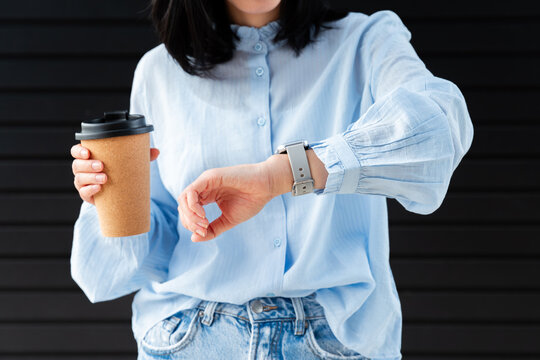 Gen Z woman checking smartwatch while holding coffee to go
