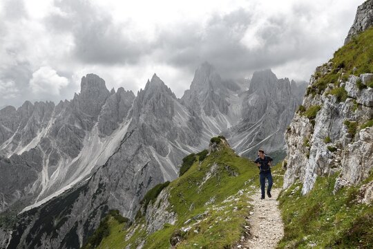 Hikers on a trail, mountain peaks and pointed rocks in the background, dramatic cloudy sky, Cimon di Croda Liscia and Cadini group, Auronzo di Cadore, Belluno, Italy