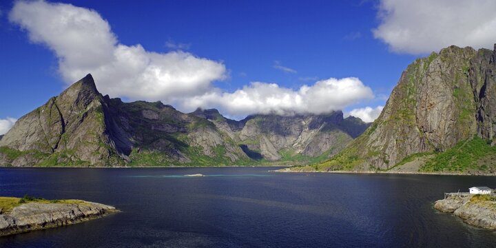 Impressive mountains under a blue sky with white clouds next to a calm fjord, Reinefjord, Hamnoy, Moskenes Lofoten, Nordland, Norway