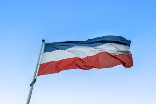 Flag of Schleswig Holstein flying against blue sky