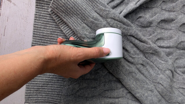 Woman's hand using an electric fabric shaver to remove lint and pilling from a sweater. 