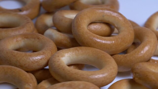 Close-up of a pile of small ring-shaped bread rolls rotating on a white plate, showcasing their smooth golden-brown crust under bright studio lighting.