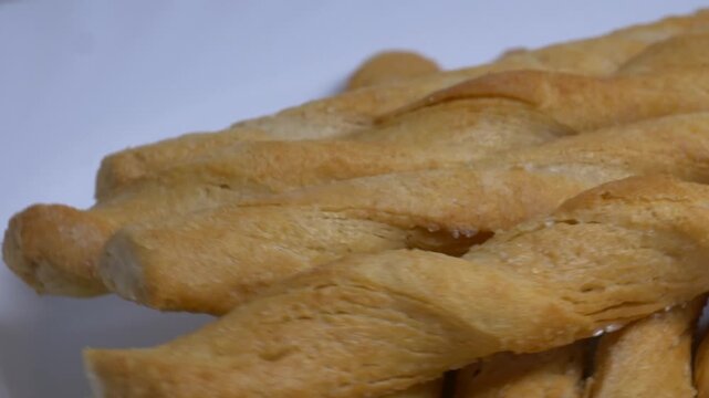 Close-up of crispy twisted puff pastry breadsticks rotating on a white plate, showcasing their golden flaky texture under bright studio lighting.