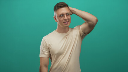 Fototapeta premium Man with hand on head, wearing glasses and beige tee, exposed forearm visible against studio backdrop; calm reflection.