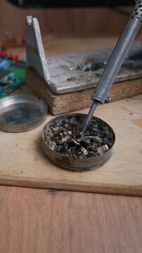 A hot soldering iron tip with molten solder dips into dark rosin flux on a wooden workbench. Concept of electronics repair, manual crafting, hardware engineering, and DIY hobby.