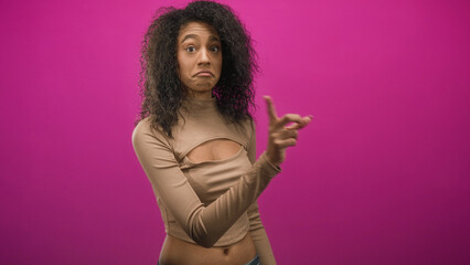 Obraz premium Woman points finger toward camera showing bare navel and midriff in pink studio backdrop; skepticism playfulness.
