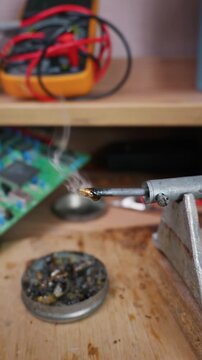 A hot soldering iron tip is dipped into a metal container of dark rosin on a wooden workbench. Concept of electronics repair, hardware assembly, DIY engineering, and manual craftsmanship.