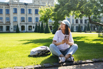 Fototapeta premium Young asian student woman smiling happy using smartphone sitting on the grass at the university campus
