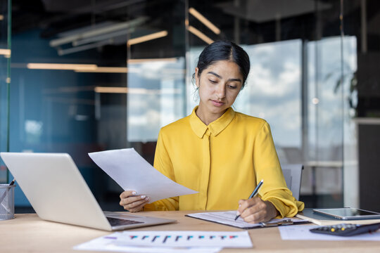 Concentrated Indian young woman checking documents in office, working with financial data