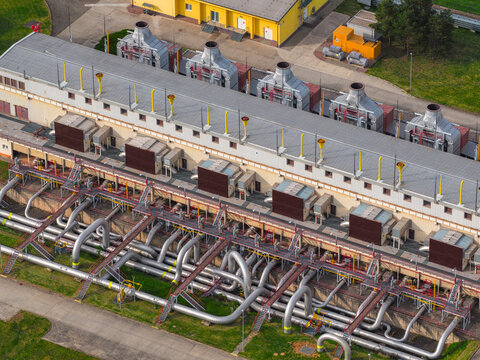 Aerial view of an industrial compressor station with complex piping, cooling units, yellow ventilation stacks, and a long building in Hrusky, South Moravian Region, Czechia.