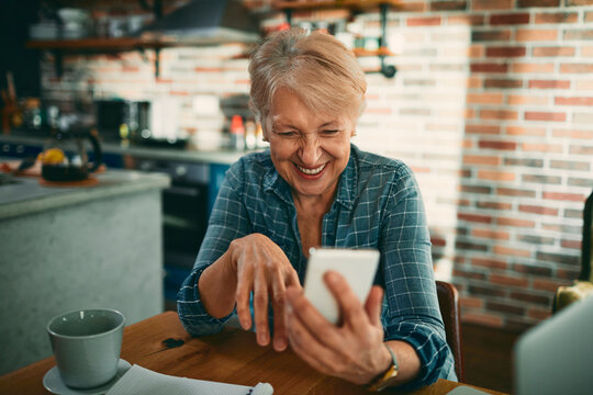 Happy senior woman video chatting on smartphone in home kitchen