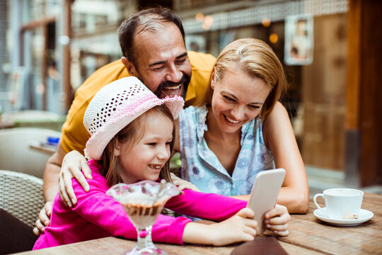 Happy family using smartphone at outdoor cafe