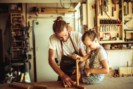 Adult teaching child woodworking in home workshop