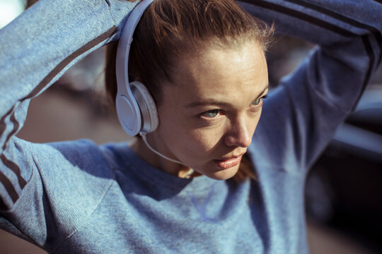 Focused young woman in headphones preparing for run outdoors