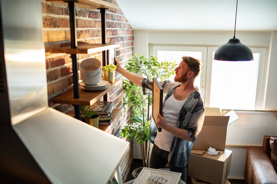 Young man arranging shelf decor in new apartment living room