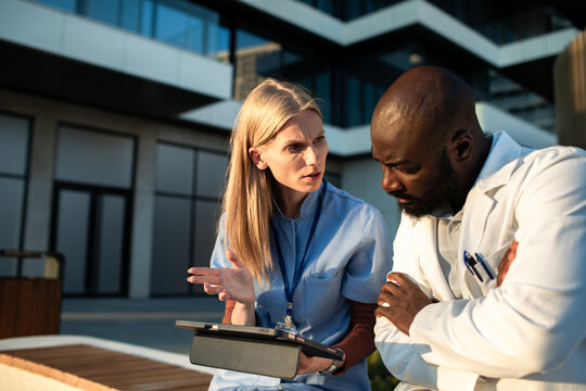 Doctor and nurse discussing patient case outside hospital with tablet