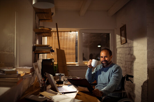 Middle-aged man in wheelchair working late at home office with coffee
