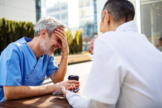 Healthcare colleagues laughing during outdoor coffee break at hospital campus