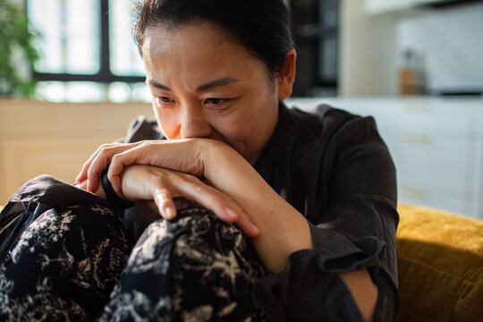 Thoughtful woman at home feeling worried on sofa