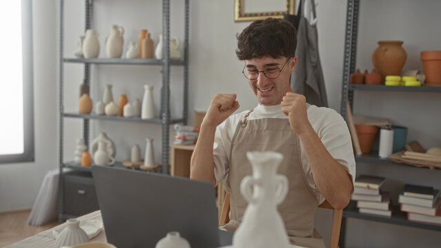 Man typing on laptop in studio surrounded by pottery and shelves, hands on keyboard showing concentration; creative satisfaction.
