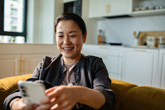Smiling woman using smartphone at home in modern kitchen