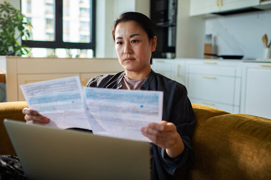 Woman reviewing household bills with laptop at home