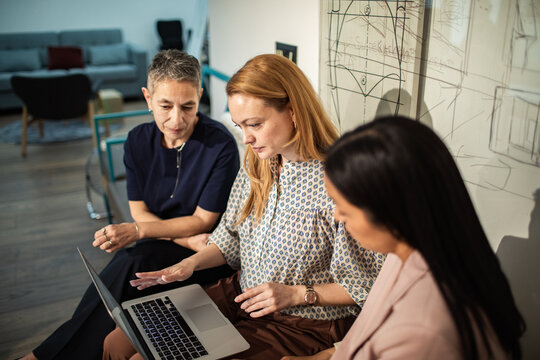 Three businesswomen collaborating on a laptop in modern office