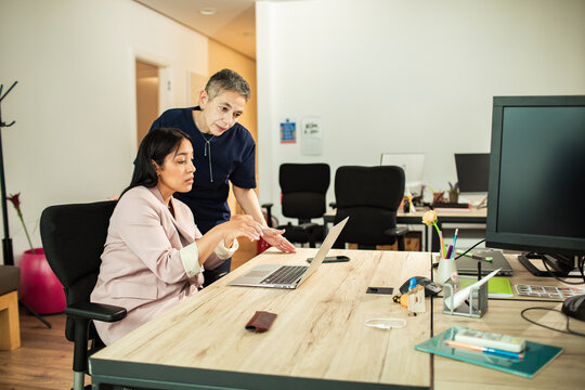 Coworkers collaborating at laptop in modern office