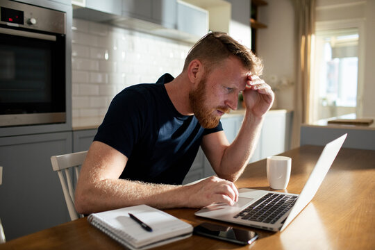 Stressed man working on laptop at home kitchen