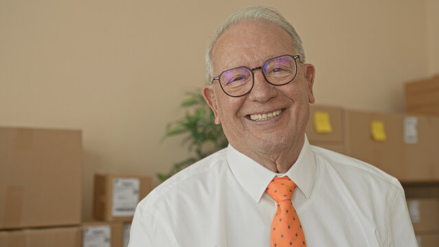 Man smiling showing teeth beside stacked cardboard boxes in a small business storage building; pride reliability.
