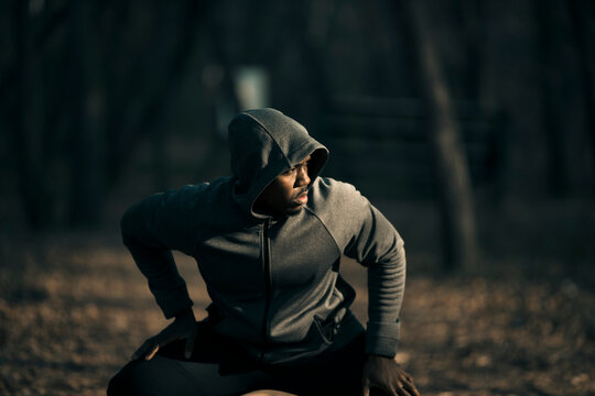 Athletic man stretching in hoodie at forest park