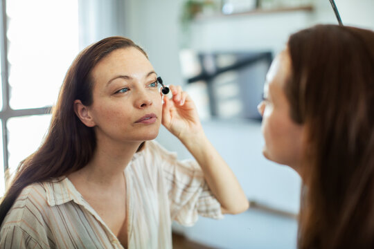 Woman applying mascara in front of mirror at home