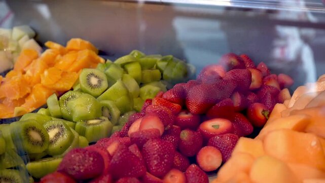 Gloved hand serving sliced fruit from colorful market display