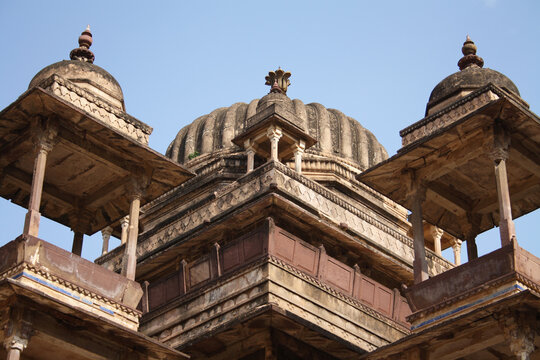 Low-angle close-up view of the ancient stone domes and intricately carved chhatris of Orchha Fort against a clear blue sky