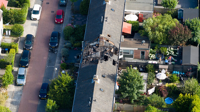 Aerial view of a residential house with a severely damaged and burnt roof structure surrounded by gardens and parked cars in Landsmeer, North Holland, Netherlands.