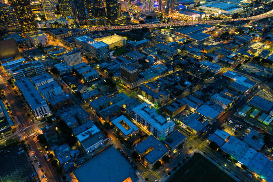 Aerial view of the illuminated city grid at night, featuring dense urban buildings, glowing street lights, and busy highway traffic in Los Angeles, California, United States.